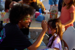 Artist painting child's face at outdoor event.