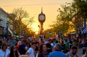Crowded downtown street festival at sunset with clock tower.